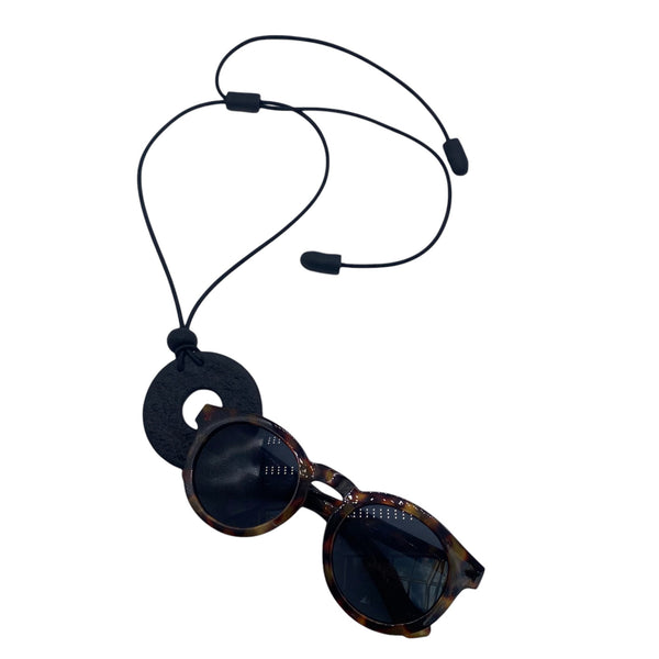 Black polymer clay statement necklace and glasses holder holding sunglasses on a white background