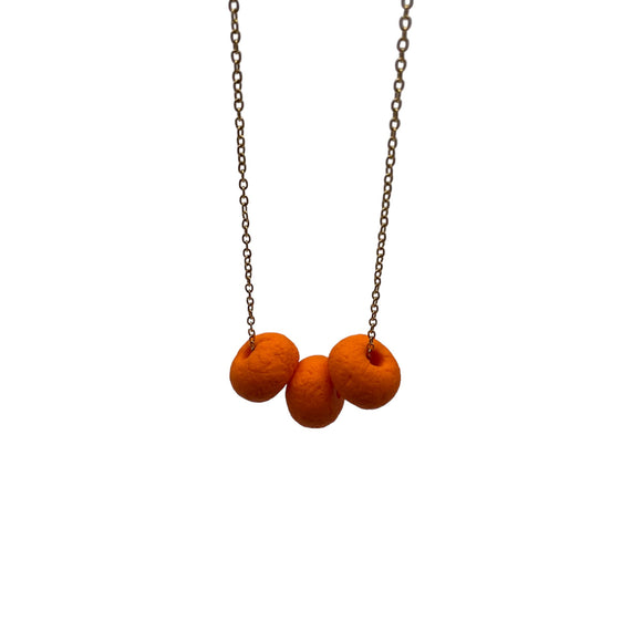 Orange polymer clay beads on a gold plated stainless steel chain on a white background