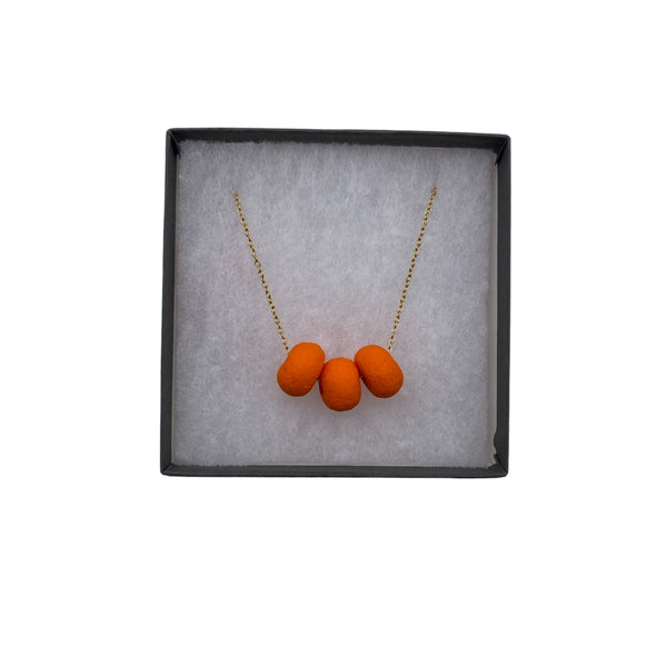 Orange polymer clay beads on a gold plated stainless steel chain in a box on a white background