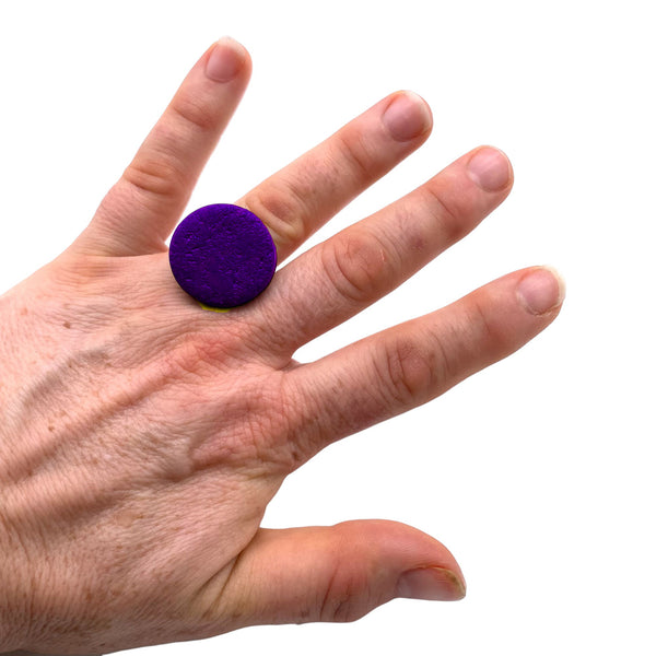 Someone wearing a Purple small polymer clay ring on a white background