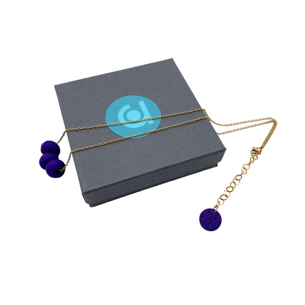 Purple polymer clay beads on a gold plated stainless steel chain on a box on a white background