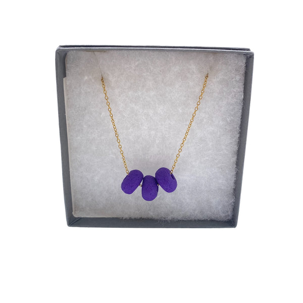 Purple polymer clay beads on a gold plated stainless steel chain in a box on a white background