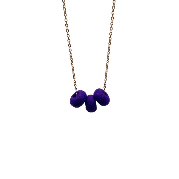 Purple polymer clay beads on a gold plated stainless steel chain on a white background