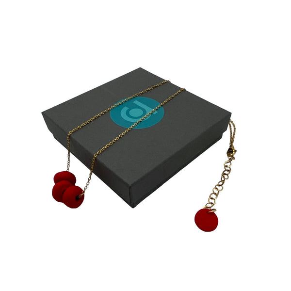 Red polymer clay beads on a gold plated stainless steel chain on a box on a white background