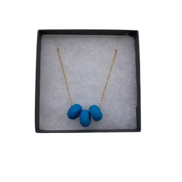 Turquoise polymer clay beads on a gold plated stainless steel chain in a box on a white background