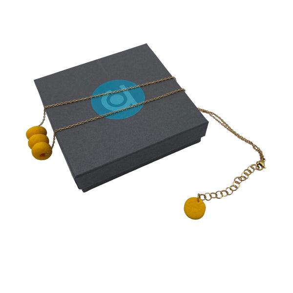 Yellow polymer clay beads on a gold plated stainless steel chain on a box on a white background