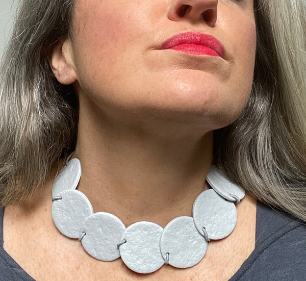 Someone wearing a Grey polymer clay statement necklace with overlapping discs on elastic cord