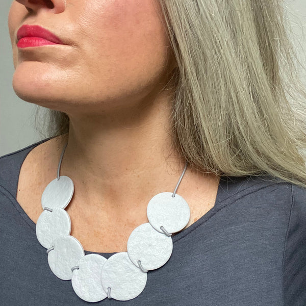 Someone wearing a Grey polymer clay statement necklace with overlapping discs on elastic cord