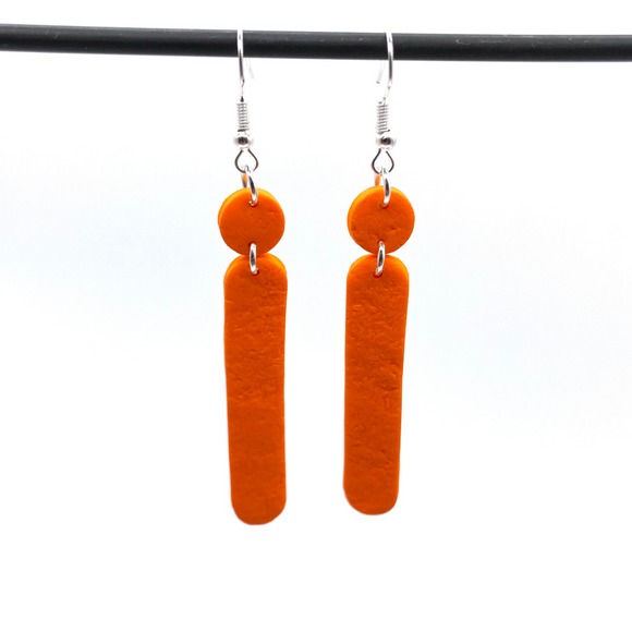 Orange Polymer Clay Dangle earrings with shepherd hooks dangling from a dark hanger