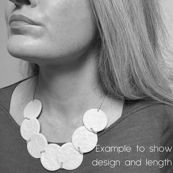 Someone wearing a polymer clay statement necklace with overlapping discs on an elastic cord. Image is in black and white to show design and size.