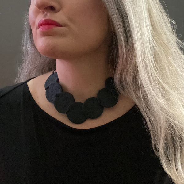 Someone wearing a black Polymer Clay statement necklace with overlapping discs